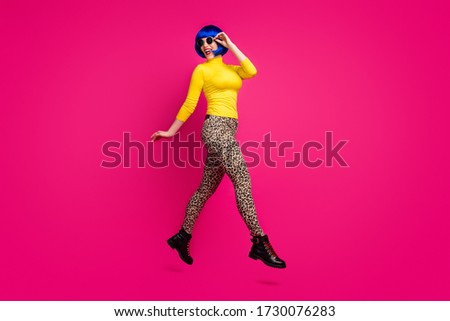 Full length profile photo of cheerful lady jumping high walk street cool traveler wear specs yellow turtleneck blue short wig boots leopard pants isolated bright pink color background