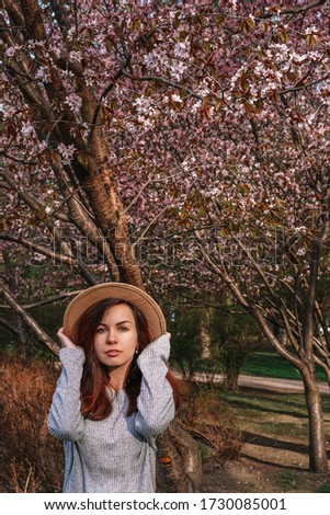 A girl with long hair in a wide-brimmed hat walks in a blooming garden, spring blooming pink cherry trees