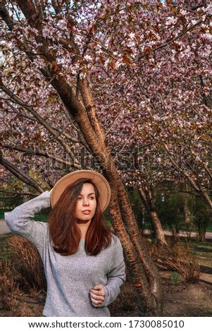 A girl with long hair in a wide-brimmed hat walks in a blooming garden, spring blooming pink cherry trees