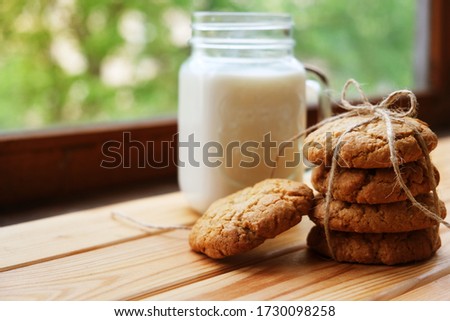 homemade oatmeal cookies tied with a thread, next to a jar of milk. It lies on a light wooden background. rustic style