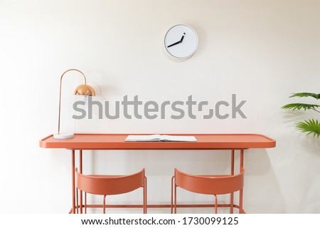 front view of orange study desk or workplace with metal electrical table lamp and white minimalist clock without numbers hanging on the wall Royalty-Free Stock Photo #1730099125