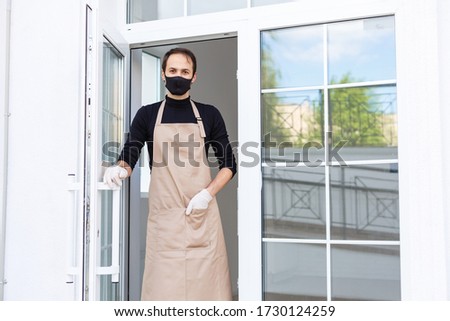 Business owner in medical mask puts on the front door due to the coronavirus COVID19 pandemic. Small business incurs losses during the coronavirus.