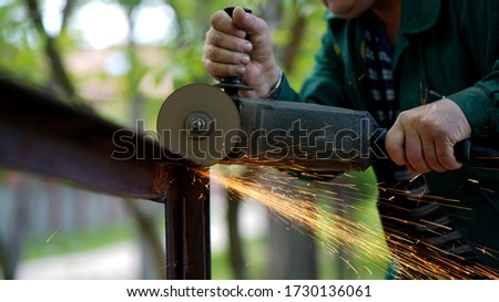 Craftsman sawing metal with disk grinder outdoors with sparks around. Electric wheel grinding on