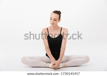 Image of caucasian young woman ballerina practicing and stretching her body isolated over white wall background