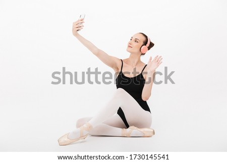 Image of caucasian young woman ballerina in headphones taking selfie photo on cellphone isolated over white wall background