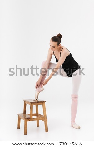Image of caucasian young woman ballerina stretching her body using chair isolated over white wall background
