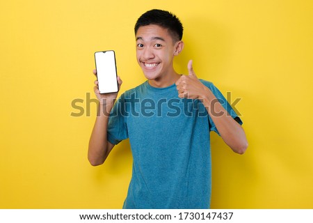 Happy Young Asian teenager showing white phone screen at the camera with okay sign, isolated on yellow background