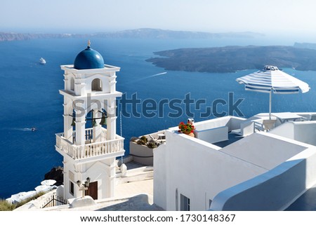 The tower of Anastasi church and parasol with ocean and islands in the background on a sunny cloudless day, Imerovigli, Santorini, Greece