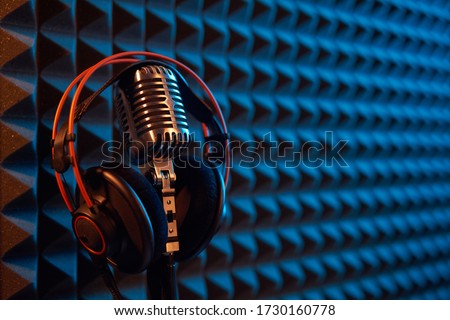 Studio condenser microphone with professional headphones on acoustic foam panel background with blue and orange light, copy space on right Royalty-Free Stock Photo #1730160778