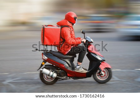 Food delivery moto scooter driver with red backpack behind back is on his way to deliver food. Courier on scooter delivering food. Quick shipping of goods to customers Royalty-Free Stock Photo #1730162416