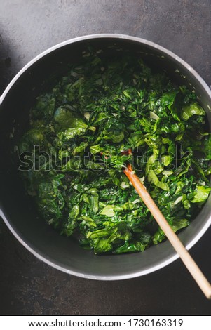 Close up of chopped stewed spinach in cooking pan with wooden spoon on rustic kitchen table. Top view. Vegetarian healthy eating concept.  Royalty-Free Stock Photo #1730163319
