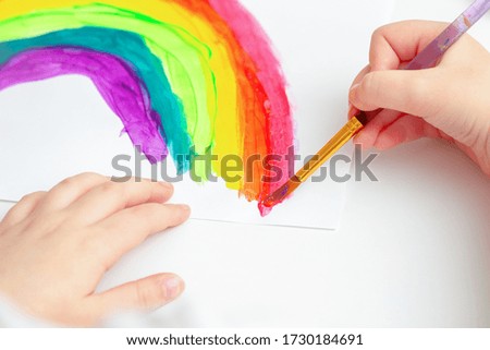 Hands of child drawing colorful rainbow by watercolors on white sheet of paper. Children's creativity concept.