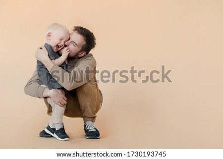 Father kissing his baby son on beige studio background. Laughing and hugging family. Father's Day
