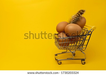 Eggs. Five brown eggs in a mini supermarket trolley and feather on an orange background close-up. Copy space.