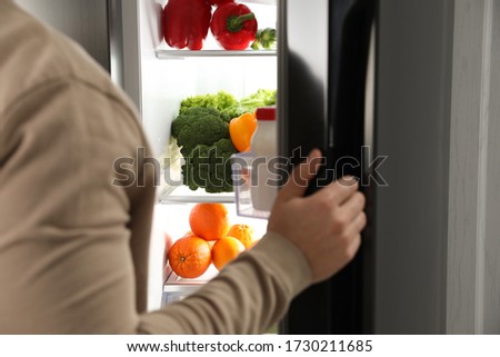 Young man opening refrigerator at home, closeup