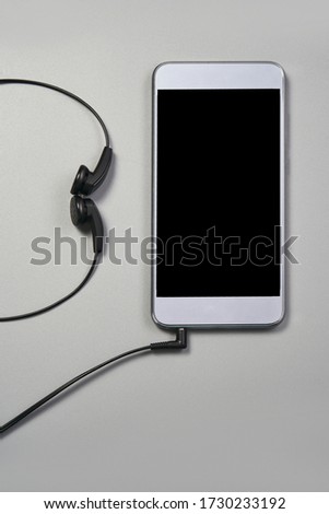 Podcast concept. Phone and earphones. Grey background. Music top view. Audio technology. Hipster lifestyle. Mockup black screen. Digital culture. School homework. Lockdown accessory