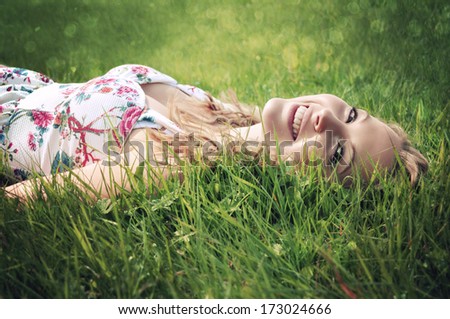 Portrait of a young smiling blonde woman lying on green grass.
