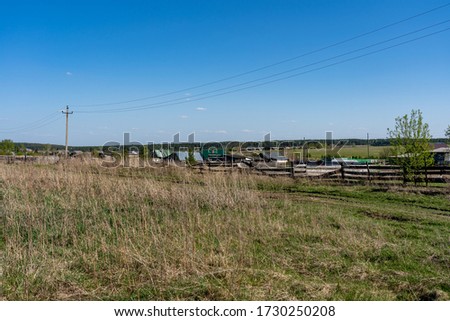 Picture of a rural landscape with old rickety wooden fence, meadow, electric line and blue sky at spring