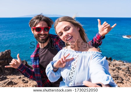 close up and portrait of two beautiful and happy people taking a selfie picture together at the beach with an islan and the sea at the background - funny and happy photo of t heir vacations and travel