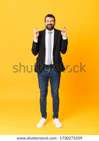 Full-length shot of business man over isolated yellow background with fingers crossing and wishing the best