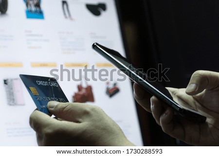 close up Shallow focus hand hold Credit Card and mobile phone with  and E-commerce website on monitor background. Background for E-commerce and online shopping concept.