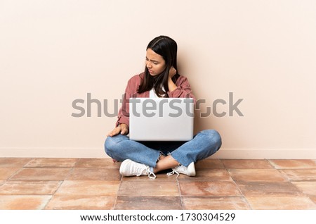 Young mixed race woman with a laptop sitting on the floor with neckache