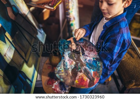 Serious young boy painting on art canvas