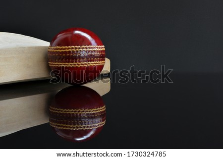 Red leather cricket ball placed Leaning against the cricket bat on a shiny black background