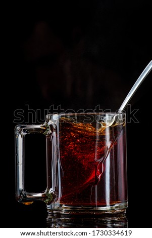 dissolving and stirring sugar in tea in a transparent mug on a black background