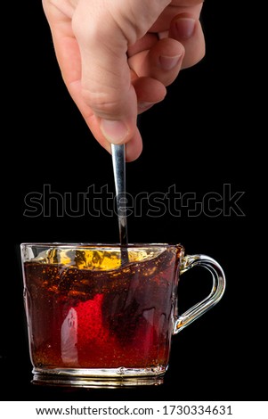 dissolving and stirring sugar in tea in a transparent mug on a black background