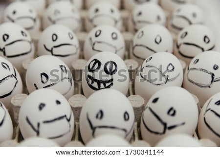 White eggs with faces drawn arranged in carton. emoticons drawn with a black marker. Smile with big teeth and narrow pupils on the background of masked eggs. coronovirus pandemic