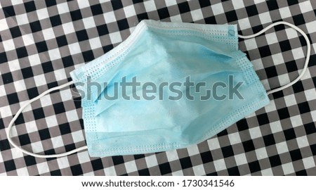 Disposable blue medical face mask with elastic bands on the sides. Mask on the background of checkered fabric. View from above.