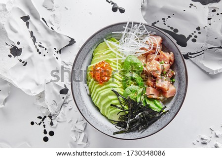 tuna poke bowl with avocado, spinach, red caviar and crispy dried seaweed among splinters of white stone on white background, trendy asian food, summer menu, terrific hot weather food, top view