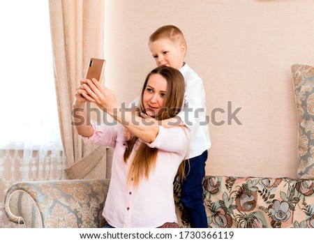 Mom and baby taking a selfie in a cozy living room. mom and son make funny faces and take pictures of themselves on camera