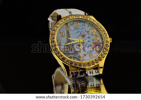 The picture shows a studio shot of a wristwatch with a gold rim set with beautiful stones.
The clock face shows an image of the Eiffel Tower