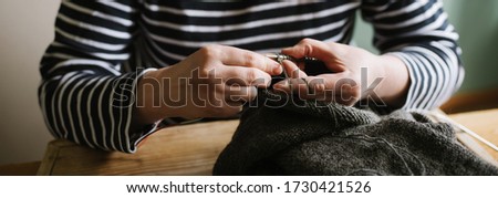 Close up photo of woman's hands knitting on grey yarn on wooden background. Top view. Hobby, craft, handmade concept. Banner for website