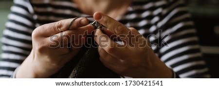 Close up photo of woman's hands knitting on grey yarn on wooden background. Hobby, craft, handmade concept. Banner for website