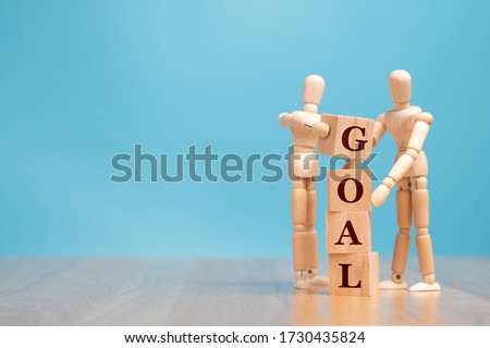 Wooden puppet standing and holding a wooden cube for making a goal word. Concept of business management must have vision and goals for drive business success and achievement