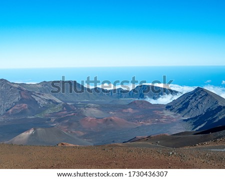 Crater walls of Maui's Haleakala Volcano with fluffy white clouds below and blue sky copy space above.