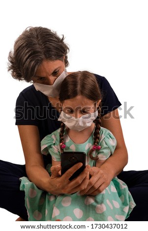 mother with her daughter on her lap wearing protective masks and looking at cell phone.