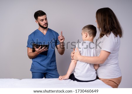 Slender pediatrician with a beard holding a folder and looking at the mother and son, the concept of consultation and treatment.