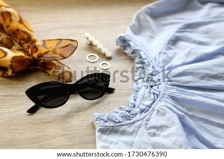Blue blouse, cat eye sunglasses, leopard print scarf and jewelry on a table. Selective focus.