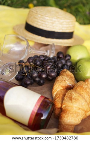 Picnic on the grass with croissant, pink wine, straw hat, grape on yellow plaid and green grass. Summer time - vertical photo