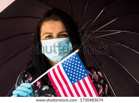 Woman with Surgical Face Masks holds flag of United States . Coronavirus Epidemic or Pandemic concept for travel, Tourism or something similar