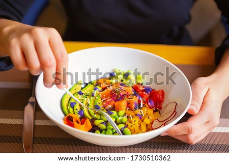 Girl eats poke bowl with salmon fish,green avocado,beans served in bowl in Asian restaurant.Vegetarian seafood cuisine for healthy eating.Delicious red fish filet,fresh vegetables.Exotic Hawaiian dish