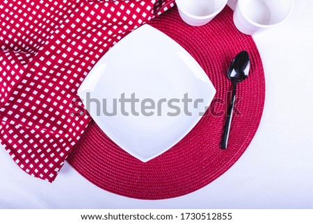 a square plate with a spoon set on a red-and-white tablecloth