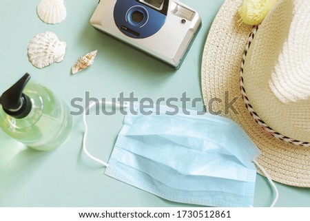 Summer tourism during coronavirus COVID-19 concept. Sun hat, camera, protective face mask, sanitizer gel for hands washing and seashells