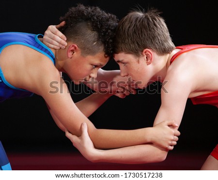 Youth wrestlers in blue and red singlets are in a collar tie on their feet