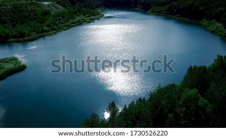 Beautiful aerial forest scene with green trees and a pond on sunny summer day. Flying over calm pond in the middle of the green forest.