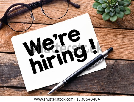 We're Hiring words written on a white sheet and a wooden background. Concept in business.